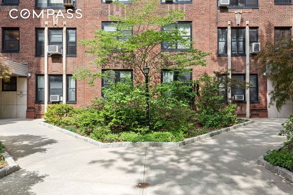 Front view of a brick apartment building with multiple windows and a small garden area in front.