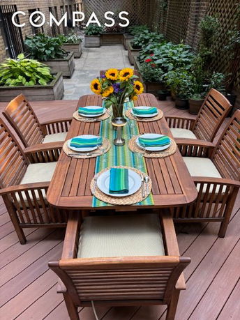 Outdoor dining area with a table set for six, surrounded by plants.