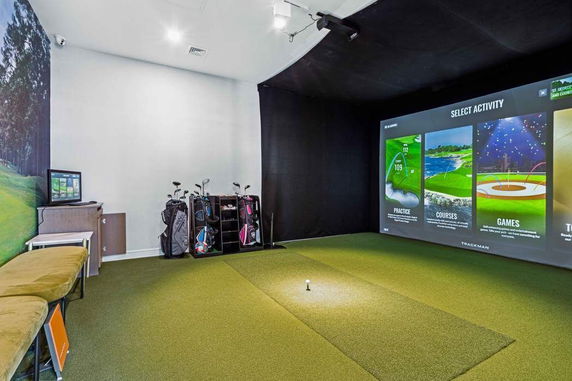 Indoor golf simulator room with golf clubs and a virtual activity screen.