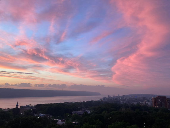 Panoramic view of a city skyline and river during sunset, with dramatic pink and blue clouds in the sky.