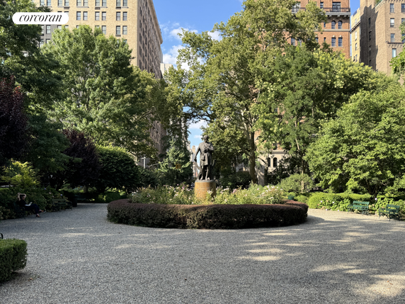 Outdoor area with a statue in the center, surrounded by trees and buildings.