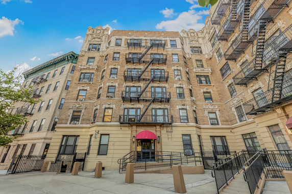 Front view of a multi-story brick apartment building with fire escape stairs.