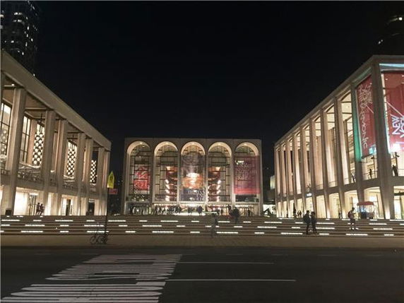 Front view of an illuminated building complex with grand archways and large glass windows at night.