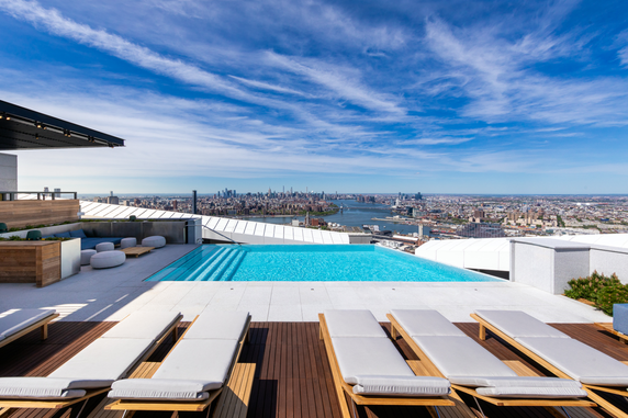 Rooftop pool area with lounge chairs and panoramic city skyline view.