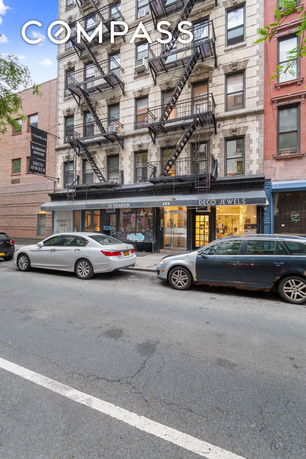 Front view of a multi-story building with fire escapes and ground floor shops.