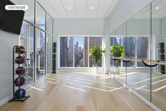 Interior view of a fitness room with exercise equipment and large windows offering a cityscape view.