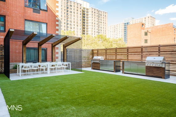 Rooftop area with a pergola, dining table, and outdoor grills on a grassy surface.