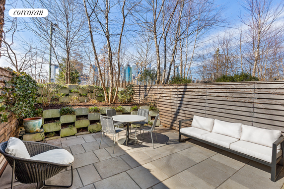 Patio area with seating and trees, view of distant buildings.