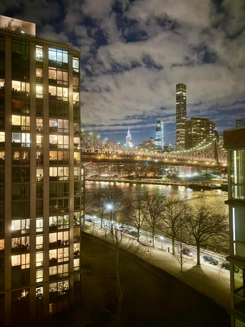 Night view of city skyline with illuminated buildings and a bridge over a river.