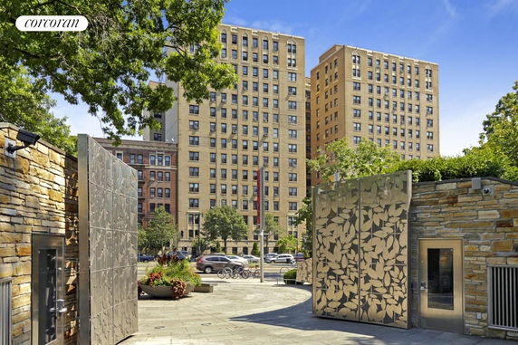 Front view of a tall apartment building with multiple windows and a decorative metallic structure in the foreground.