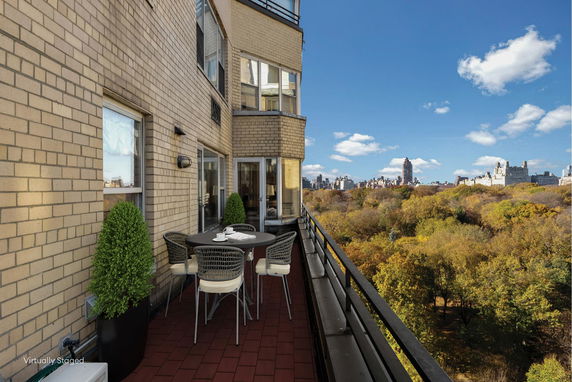 Outdoor balcony with table and chairs overlooking a cityscape and park.