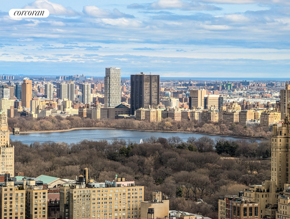 Panoramic view of a city with tall buildings and a central park area featuring a large reservoir.