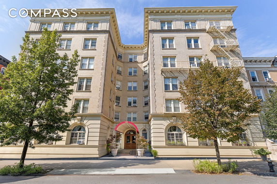 Front view of a multi-story apartment building with large windows and a red awning at the entrance.