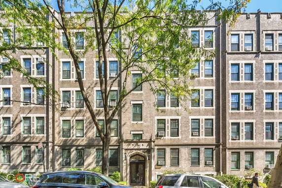 Front view of a multi-story brick apartment building with numerous windows and a central entrance.