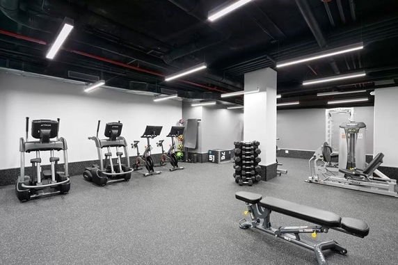 Indoor gym area with exercise equipment including treadmills, stationary bikes, weight bench, and dumbbells.