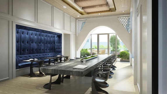 Indoor area with a long table and chairs, adjacent to a cushioned seating area.