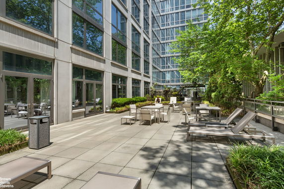 Outdoor patio area with lounge chairs and tables next to a modern building with large windows.