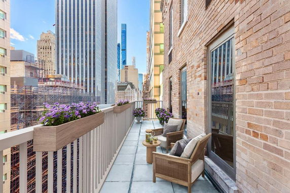 Balcony with seating area and potted plants overlooking cityscape.