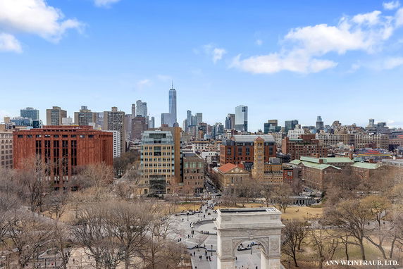 A panoramic view of a cityscape with skyscrapers and historic buildings, and a park with a prominent arch in the foreground.