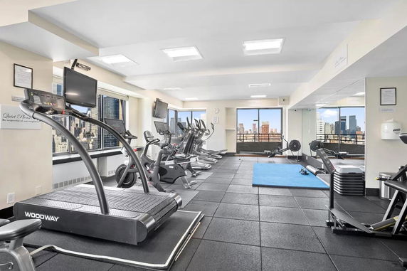 Indoor gym with exercise machines and large windows in a building.