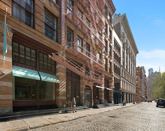 Front view of a multi-story building with a fire escape and shops at the ground level.