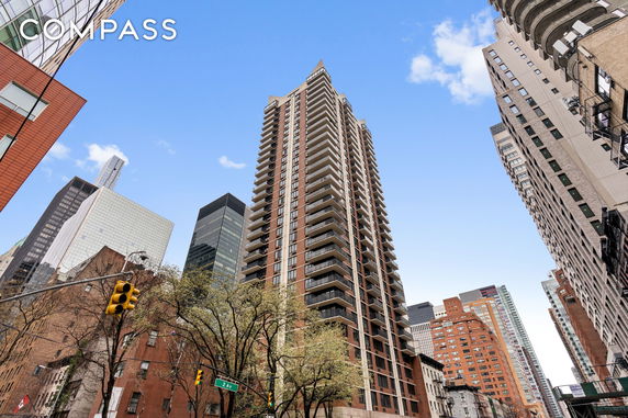 Front view of a tall residential building with multiple balconies against a cityscape background.