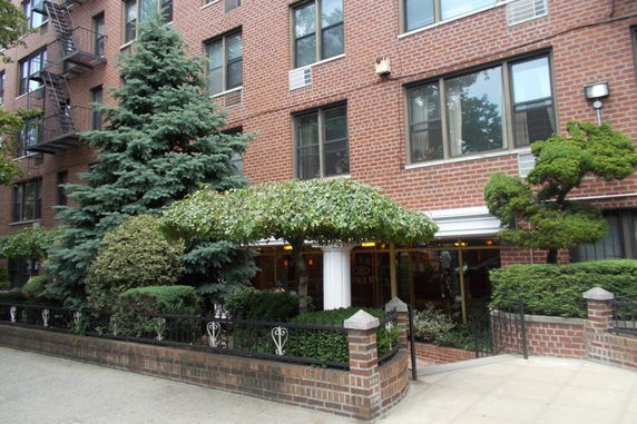 Front view of a multi-story brick building with an entrance covered by greenery and shrubs.