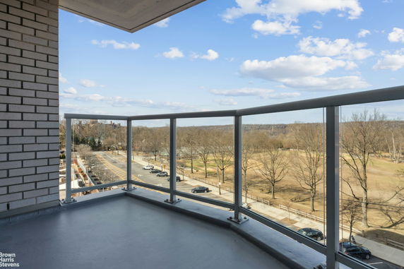 View from a balcony overlooking a park and street with trees and parked cars.