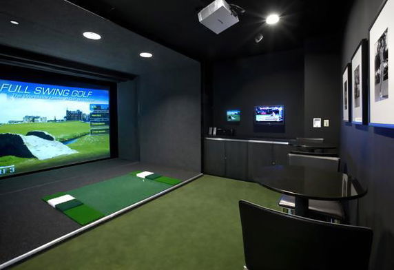 Indoor golf simulator room with seating and golf practice area.