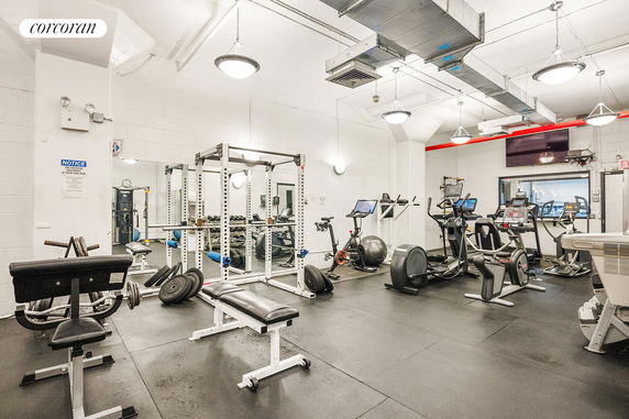 Indoor gym area with various exercise equipment including weights, benches, and cardio machines.
