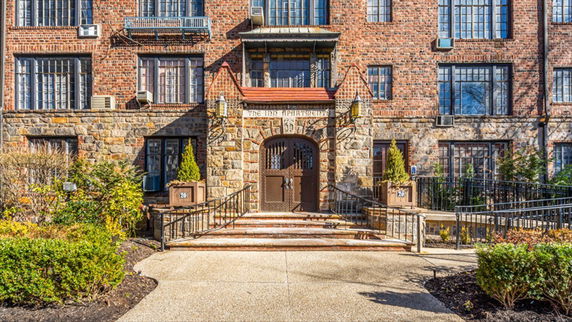 Front view of a brick apartment building with stairs leading to an arched entrance.