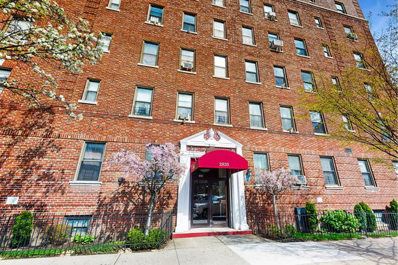 Front view of a multi-story brick apartment building with a red awning over the entrance.