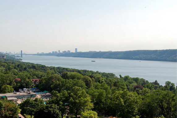 Panoramic view overlooking a river with a bridge in the background and a city skyline visible.
