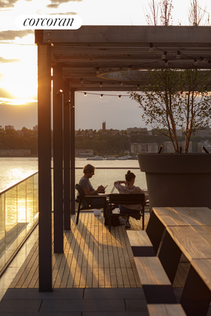 Rooftop seating area with sunlight filtering through a pergola, overlooking a water view.