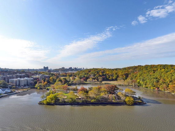 Aerial panoramic view of a river with surrounding buildings and forested area in the background.