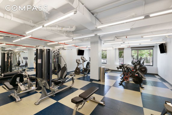 Indoor fitness club area with exercise equipment, including bikes and machines.