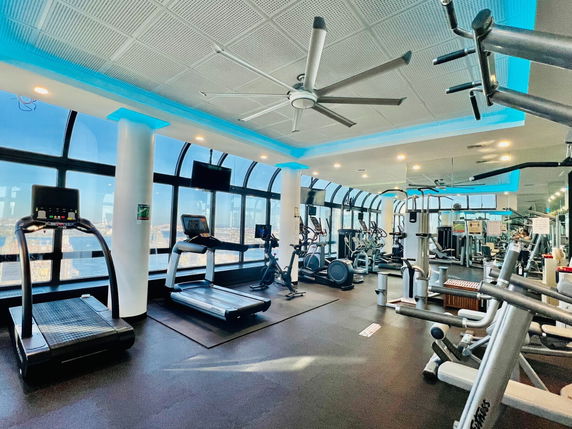 A modern gym area with various fitness equipment and large windows.