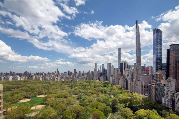 Aerial view of Central Park and surrounding skyscrapers on a sunny day with scattered clouds.