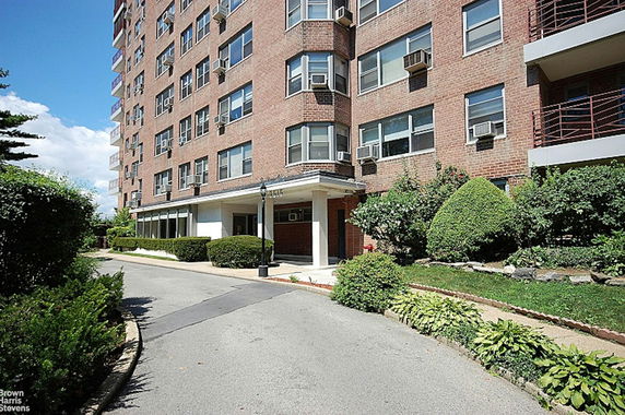 Front view of a multi-story brick apartment building with a landscaped entrance.