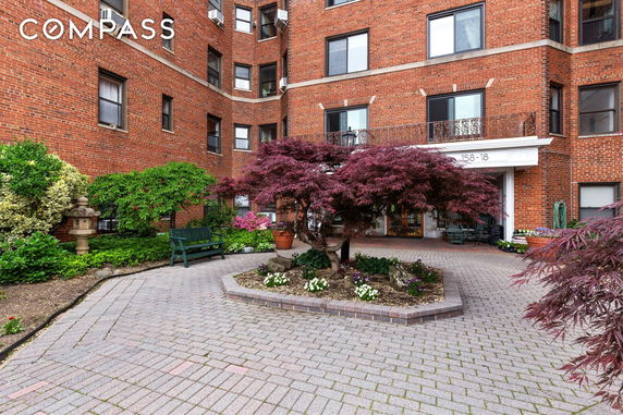 Front view of a red brick residential building with entrance and landscaped courtyard.