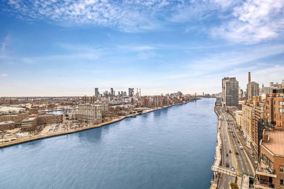 Panoramic view of a river with city buildings on both sides under a blue sky.
