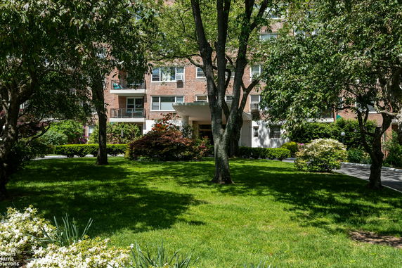 Front view of a multi-story brick residential building with balconies and landscaped garden.