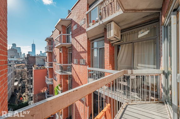 View of balconies on a red brick apartment building with a city skyline in the distance.