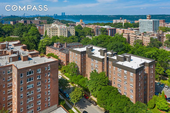 Aerial view of multiple apartment buildings with surrounding greenery and distant cityscape.