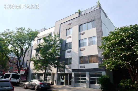 Front view of a modern multi-story building with large windows and a rooftop area.