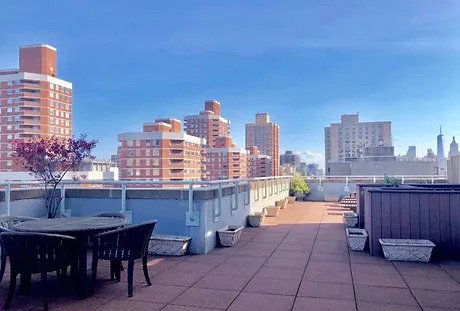 Rooftop space with a view of surrounding tall buildings, featuring seating and planters.