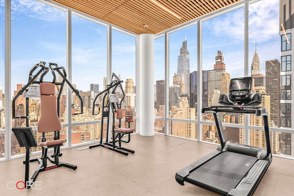 Indoor gym area with exercise equipment and large windows offering city views.