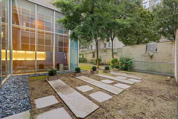 Modern building exterior with glass windows, a landscaped garden area, and decorative stone walkway.
