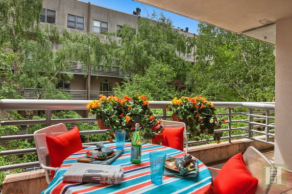 Balcony with outdoor table and chairs, overlooking green trees and residential buildings.