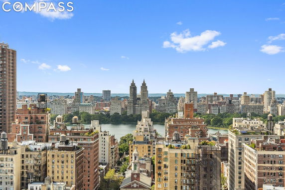 Wide angle view of a cityscape with multiple high-rise buildings and a body of water in the background under a clear blue sky.